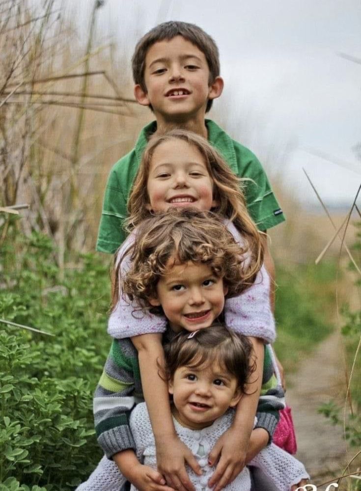 three children are sitting on top of each other in front of tall grass and bushes