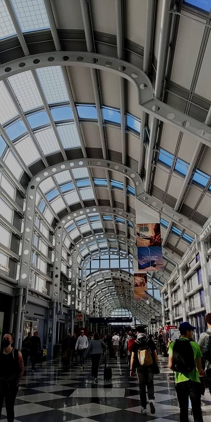 many people are walking through an indoor shopping mall with high ceilings and large windows on the ceiling