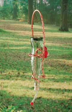 a glass wind chime hanging from a tree in the grass with trees in the background