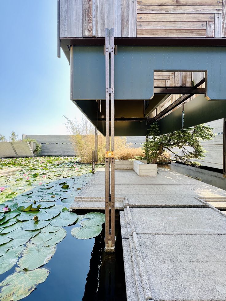 the water has lily pads on it and is next to a building with a wooden roof