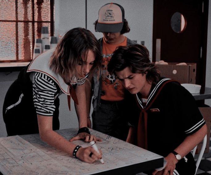 three people standing around a table with a map on top of it and one person writing