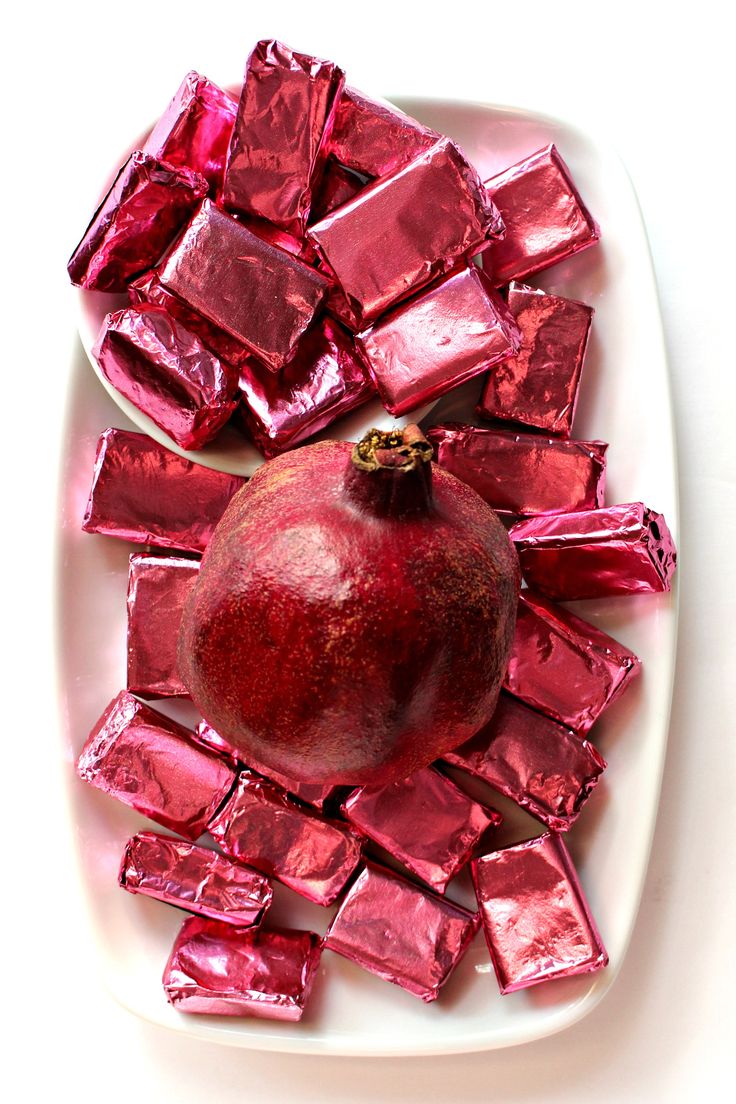 a white plate topped with a pomegranate and pieces of pink foil