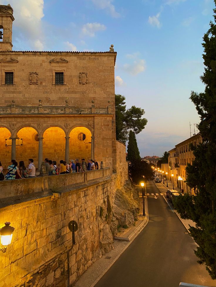 people are sitting on the ledge of an old stone building at night with street lights