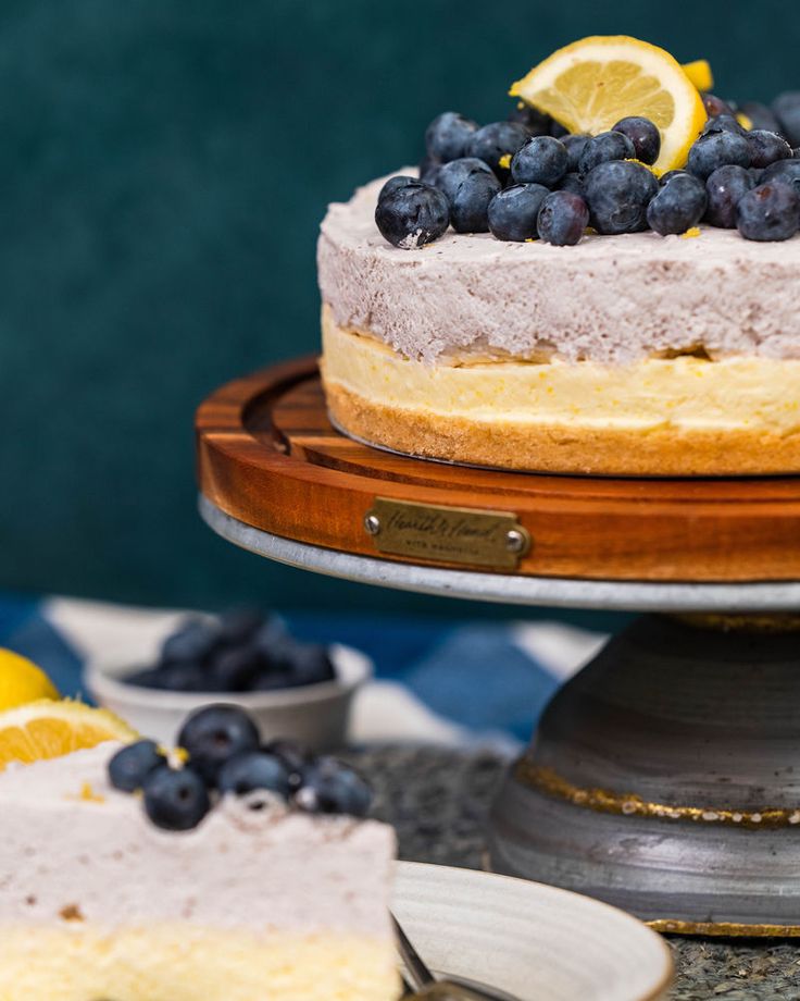 a cheesecake with blueberries and lemons on a wooden plate next to other dessert items