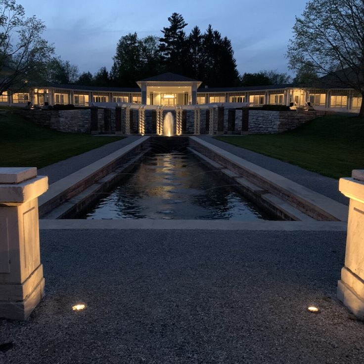 the entrance to a mansion lit up at night with water in the foreground and lights on