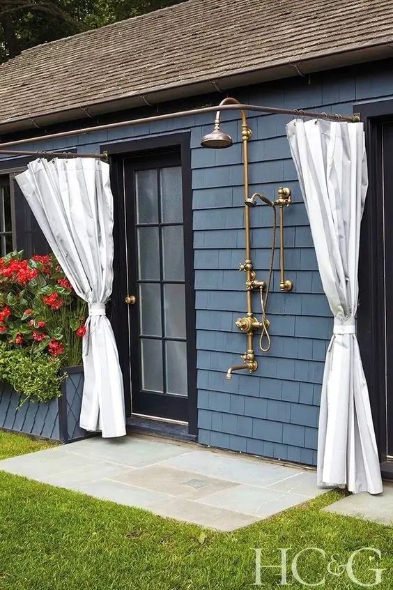 an outdoor shower with curtains on the side of it and flowers in front of it