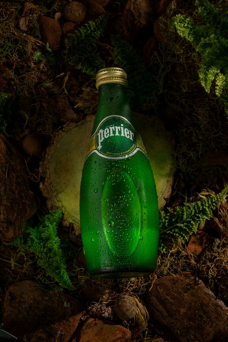 a bottle of beer is sitting on the ground next to some rocks and mossy plants