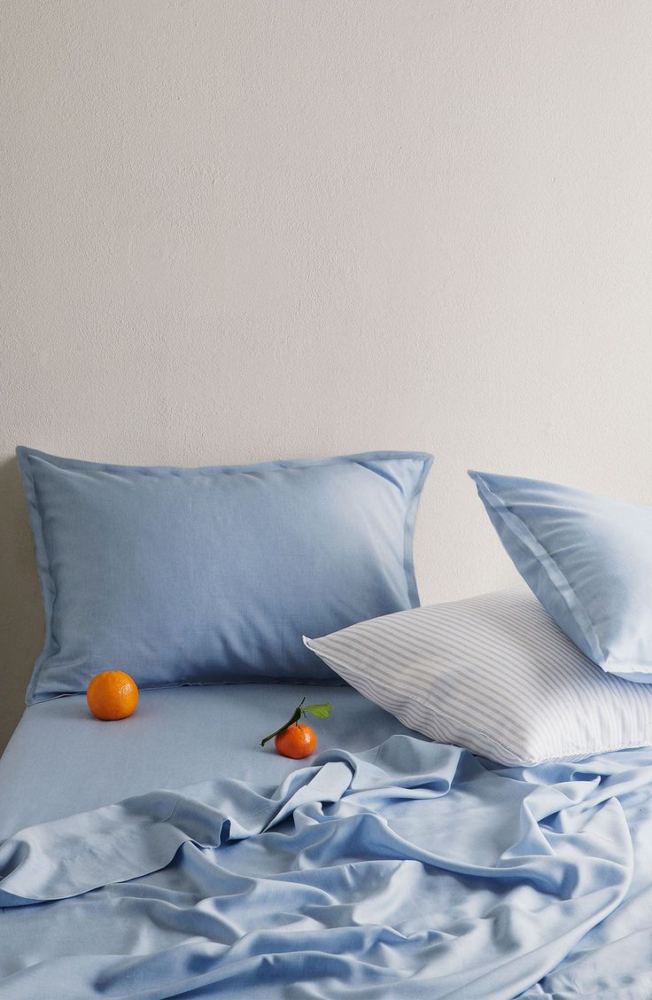 an unmade bed with blue sheets and two oranges on the pillowcase next to it