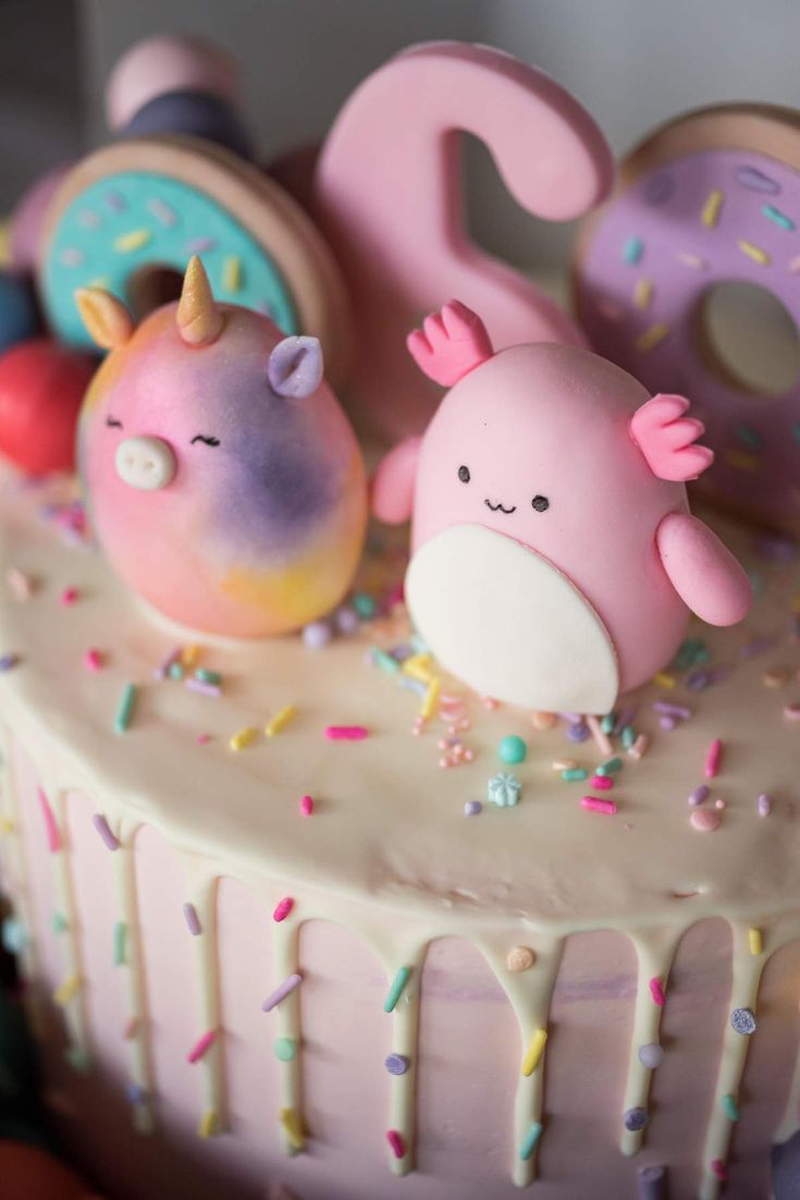 there is a pink cake with sprinkles and two animals on the top