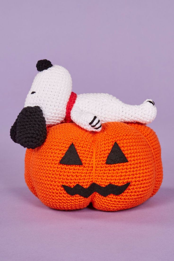 a crocheted dog laying on top of a pumpkin with a white and black nose