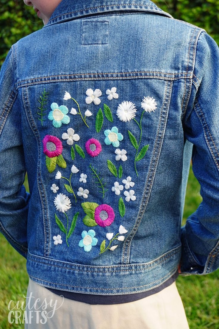 the back of a woman's jean jacket with flowers embroidered on it, in front of green grass