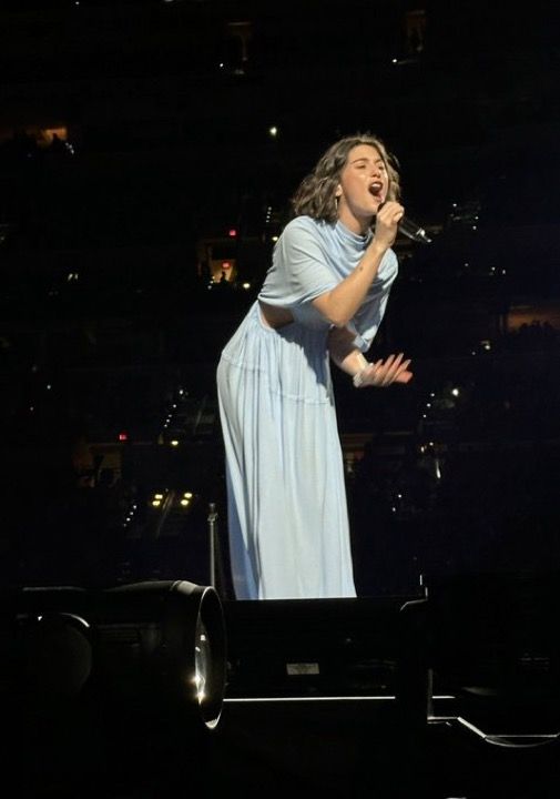 a woman in a blue dress singing on stage with her hands out to the side