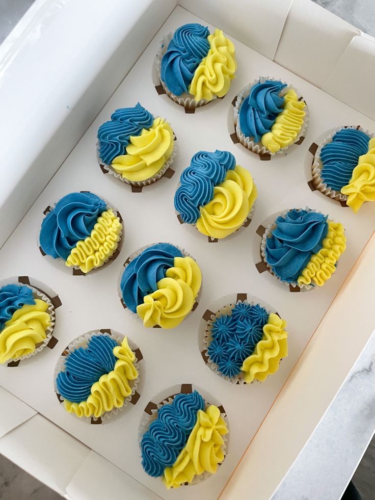 blue and yellow frosted cupcakes in a white box on a marble table