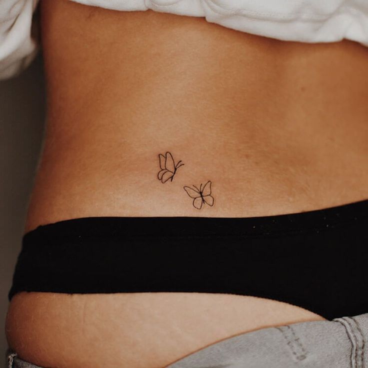 a woman's stomach with two small butterflies on the side, tattooing it