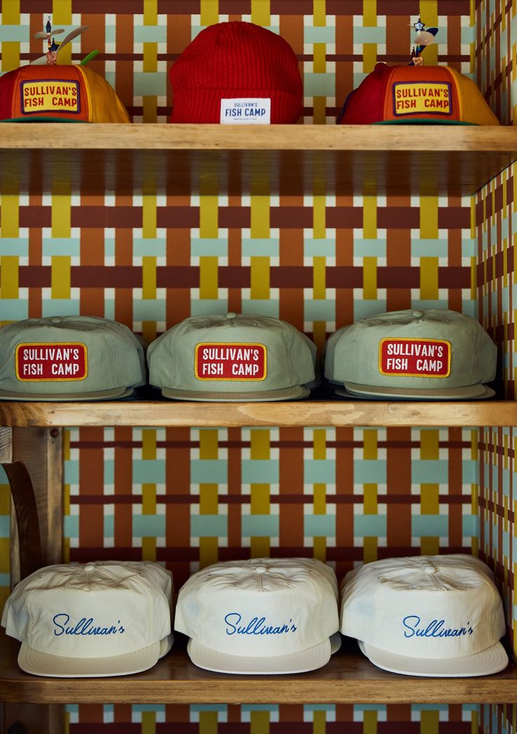 hats are on shelves in a store with colorful wallpaper behind them and below them, there is a sign that says sulleyware fish camp