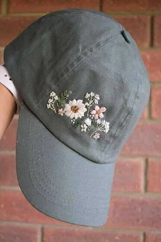 a person wearing a gray hat with flowers on the front and side, while holding it in their hand