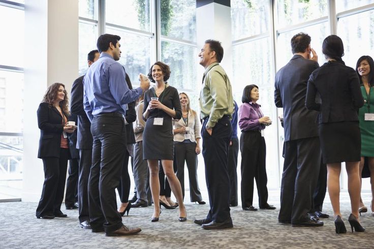 a group of people standing around each other in front of large windows and talking to each other