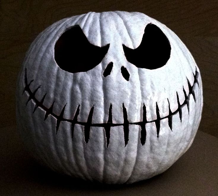 a white pumpkin with black eyes and teeth on it's face, sitting on a table