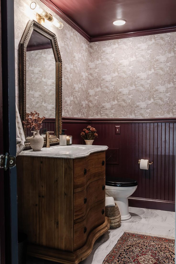 a bathroom with a toilet, sink and mirror in it's corner area next to a rug on the floor