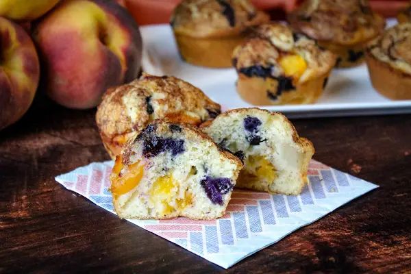 muffins with blueberries and peaches sitting on a napkin next to some peaches