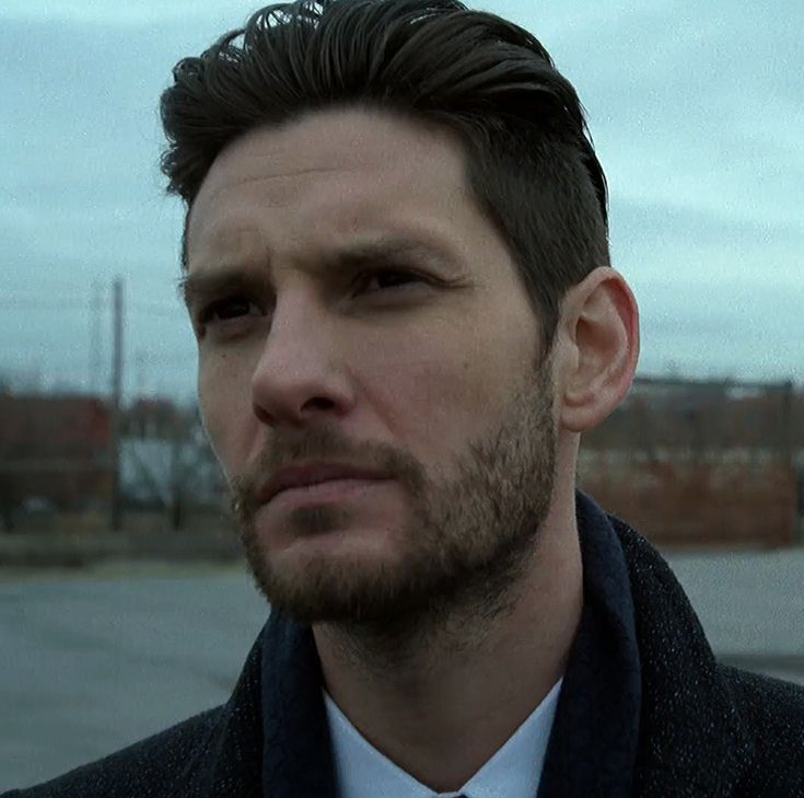 a man wearing a suit and tie standing in front of an empty parking lot on a cloudy day