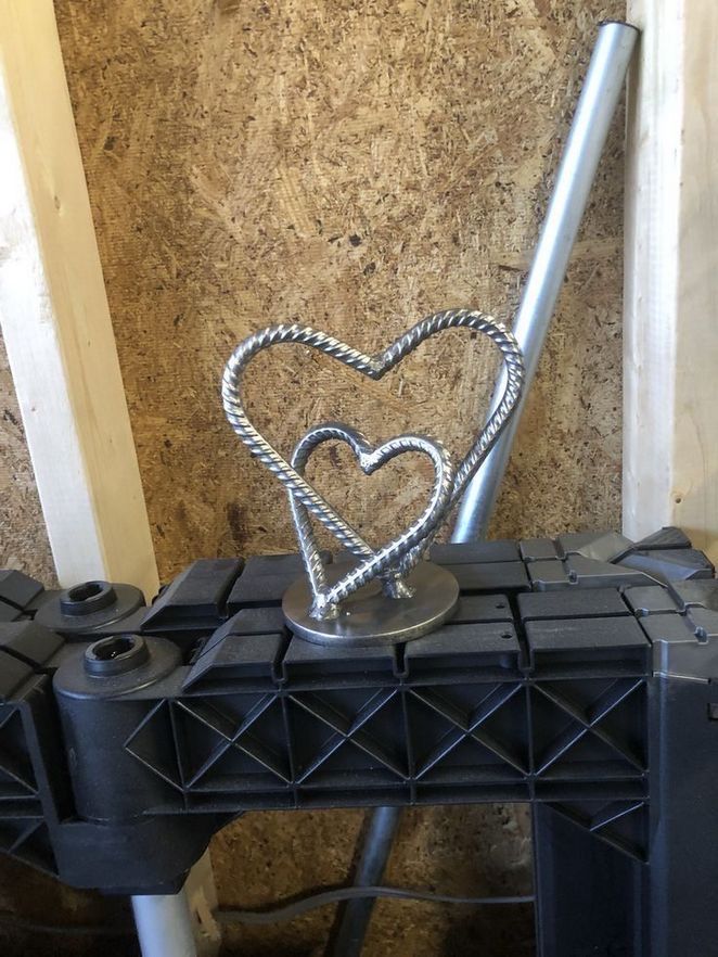 a metal heart on top of a black carton next to a wall covered in plywood