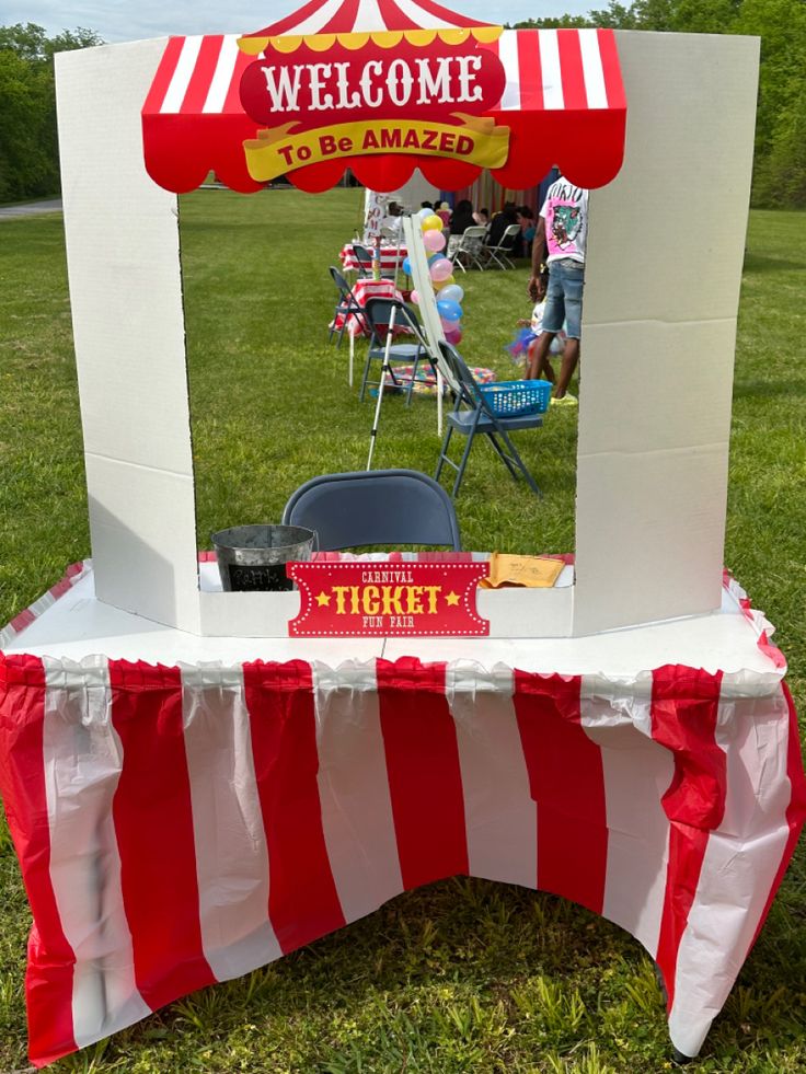 a red and white striped tent sitting on top of a grass covered field next to a picnic table