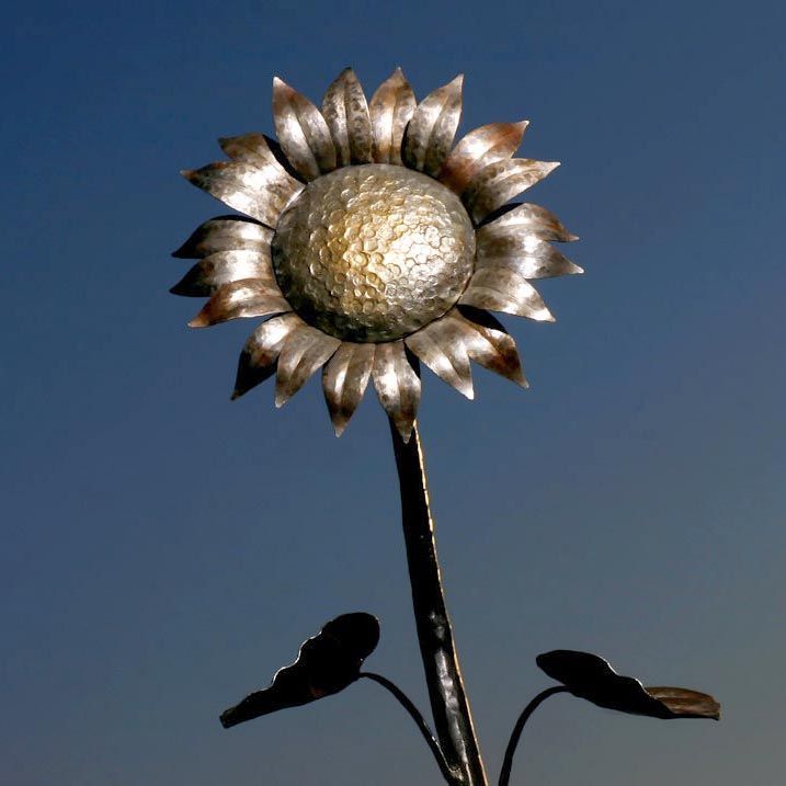 a large metal sunflower on top of a pole with sky in the back ground