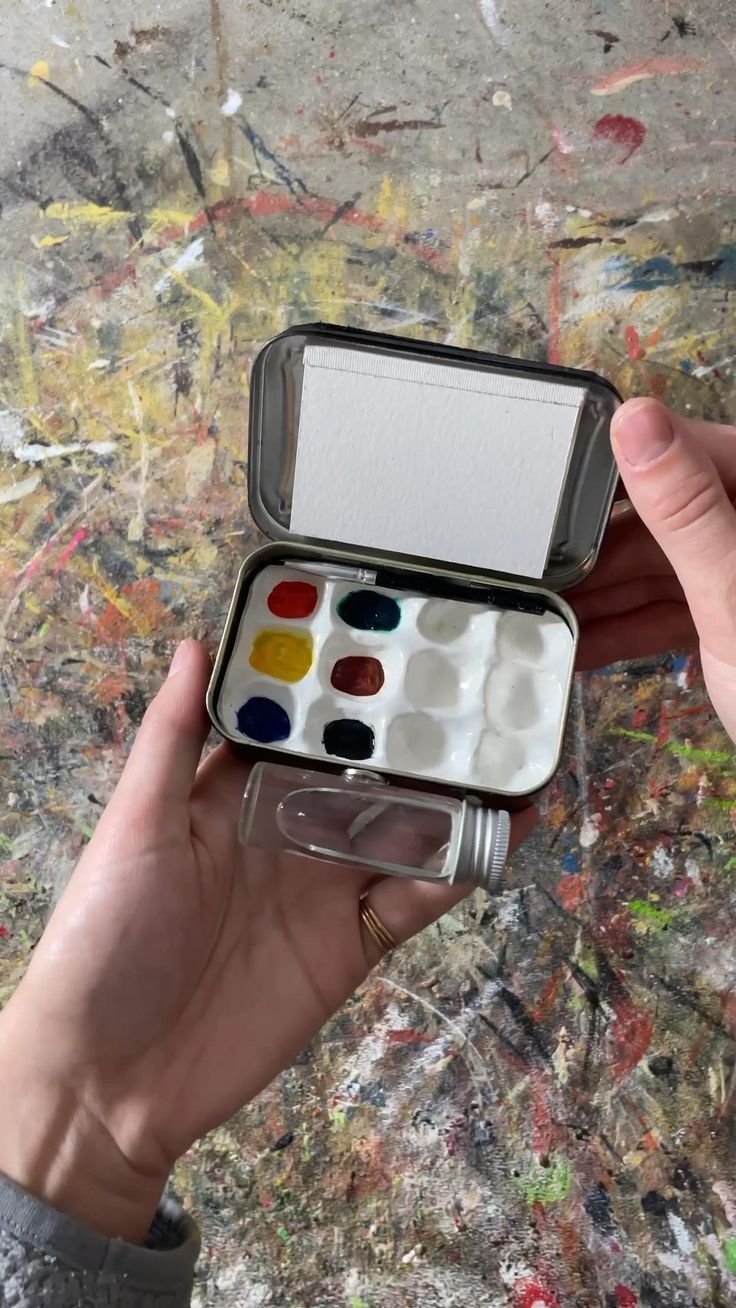 a person holding an open paint box filled with watercolors