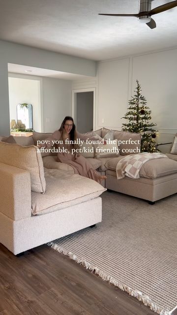 a woman sitting on top of a couch in a living room next to a christmas tree