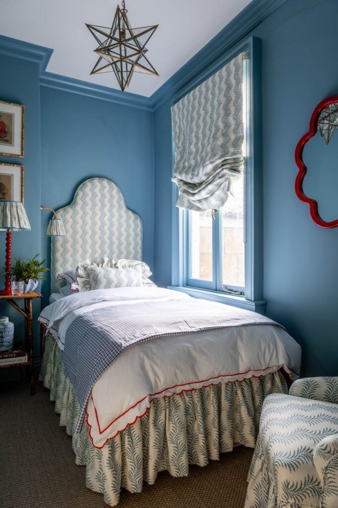 a bed sitting under a window next to a chair in a room with blue walls