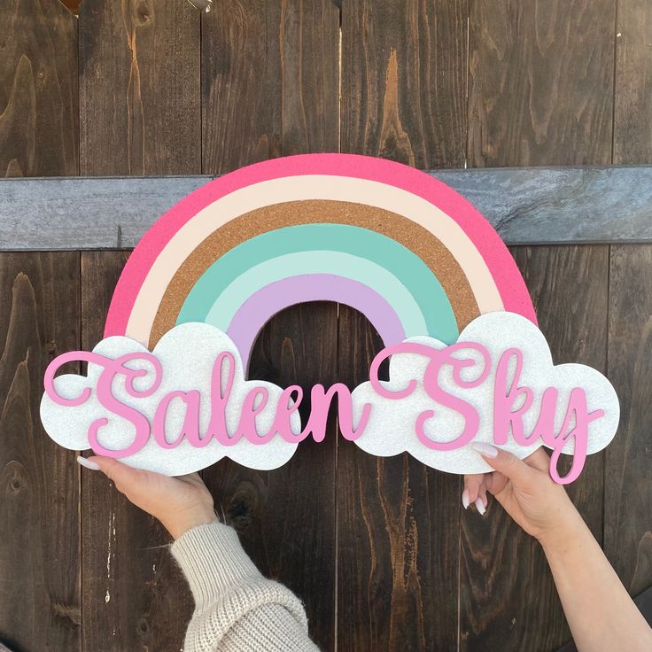 someone holding up a wooden sign with the word salem sky in front of a rainbow