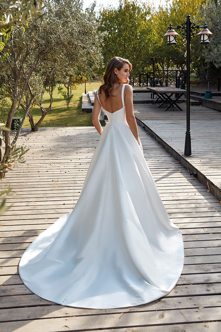 a woman in a white wedding dress is standing on a wooden walkway with her back to the camera