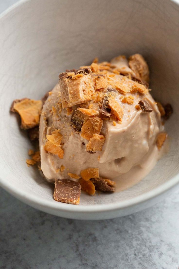 an ice cream sundae in a white bowl on a marble countertop, topped with toasted graham crackers