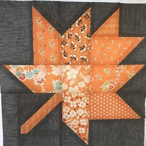 an orange and black quilted star with flowers on it's side, sitting on a gray piece of fabric