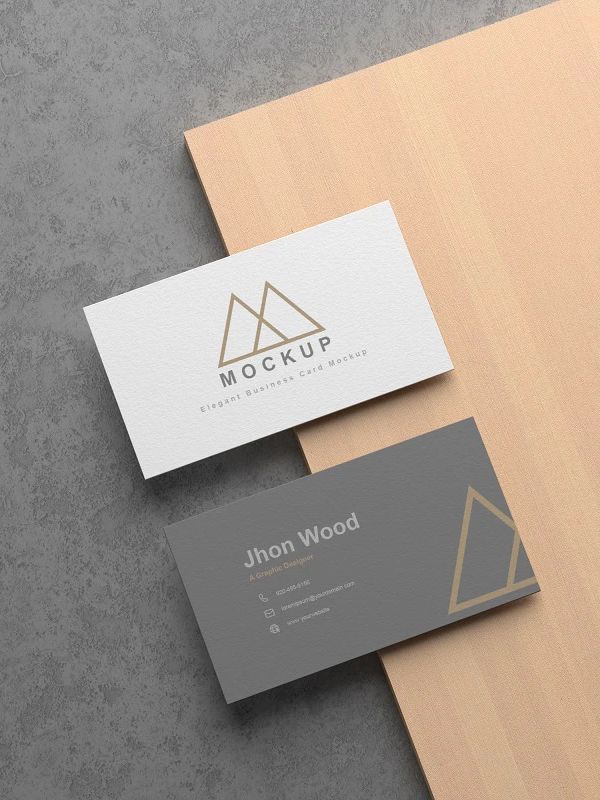 two business cards sitting on top of each other next to a wooden board with the word mockup printed on it