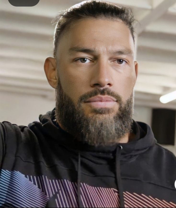 a man with a beard wearing a black hoodie and looking at the camera while standing in an office