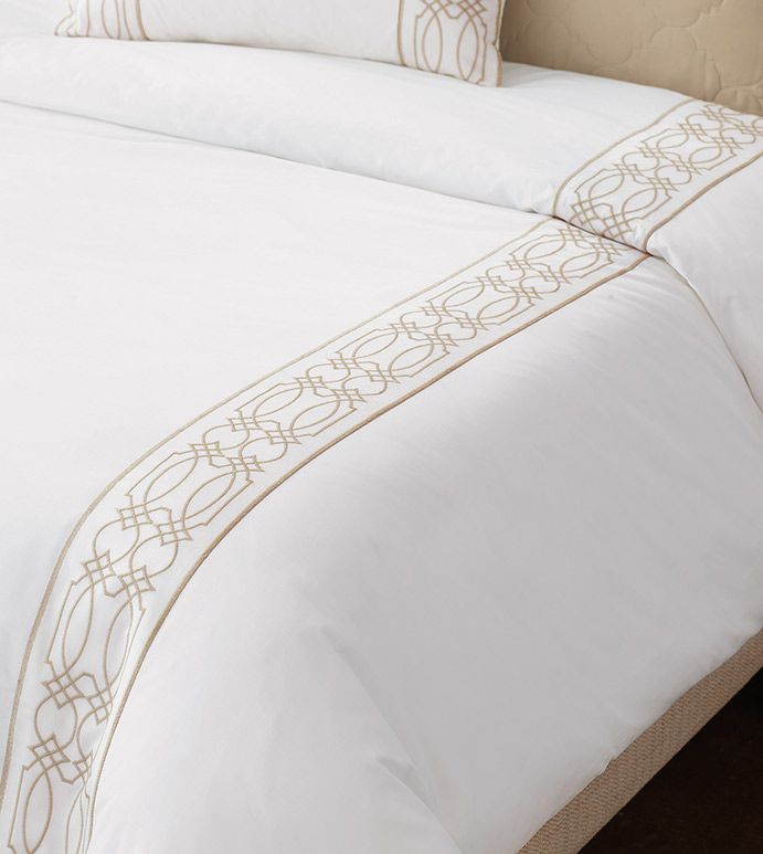 a bed with white sheets and gold trimmings