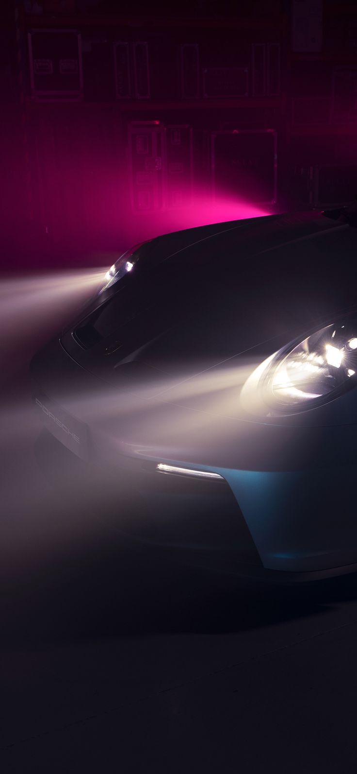 a black sports car driving down a street at night with fog coming off the hood