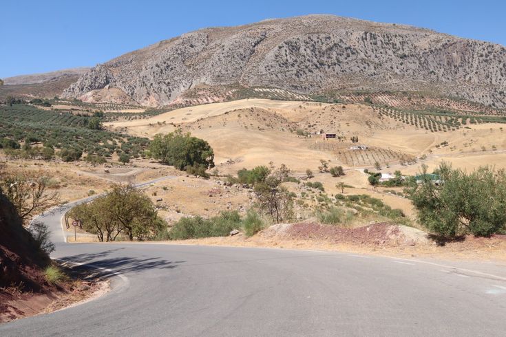 an empty road in the middle of a hilly area with hills and trees on either side