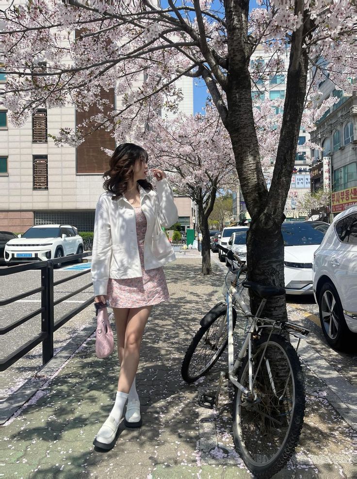 a woman walking down the sidewalk next to a tree with pink flowers on its branches