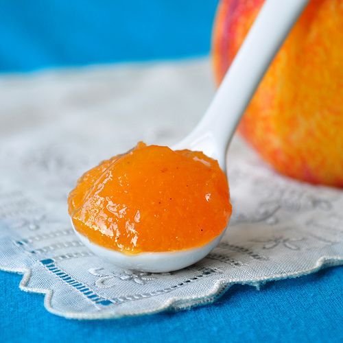 a spoon full of orange marmalade sits on a napkin next to an apple