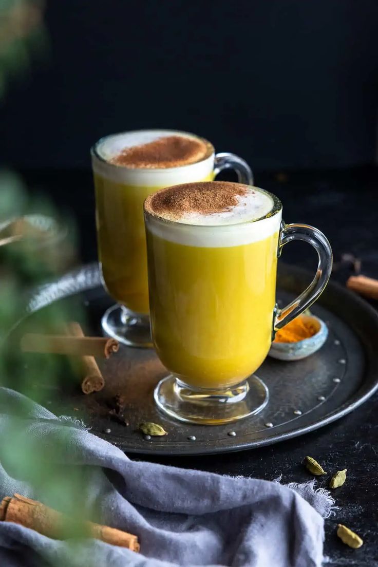 two mugs filled with hot chocolate and cinnamon sitting on a plate next to each other