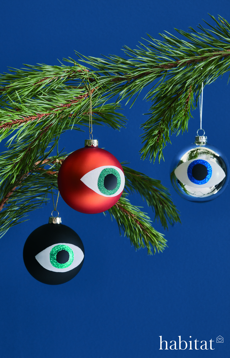 two ornaments hanging from a pine tree with an evil eye ornament on it