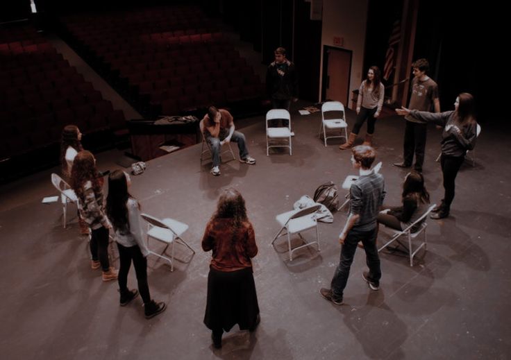 a group of people standing around each other in a circle with chairs on the floor