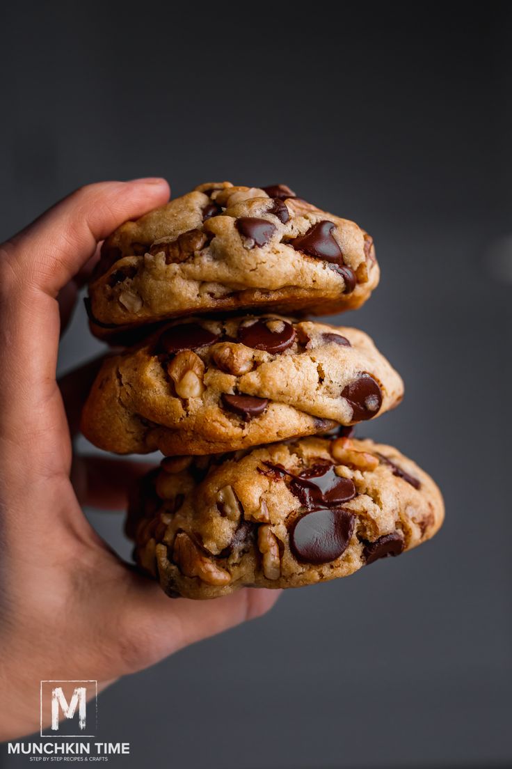 a hand holding three chocolate chip cookies on top of each other