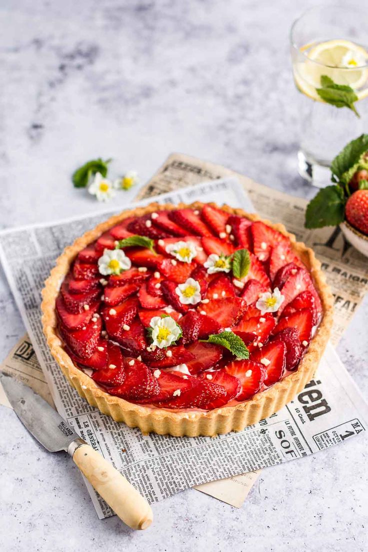 a strawberry tart on top of a newspaper next to a bowl of strawberries