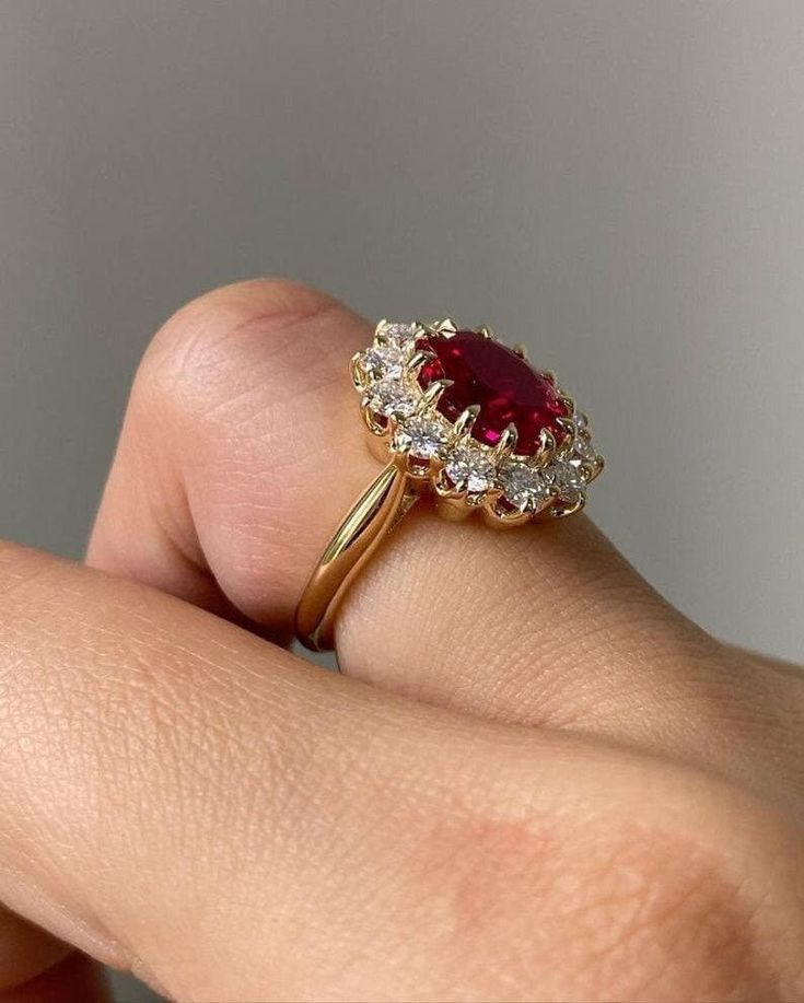 a woman's hand holding a ring with a red and white stone in it