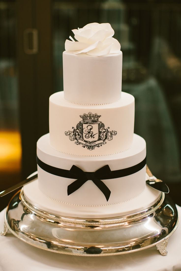 a three tiered wedding cake with black ribbon and white rose on top is sitting on a silver platter