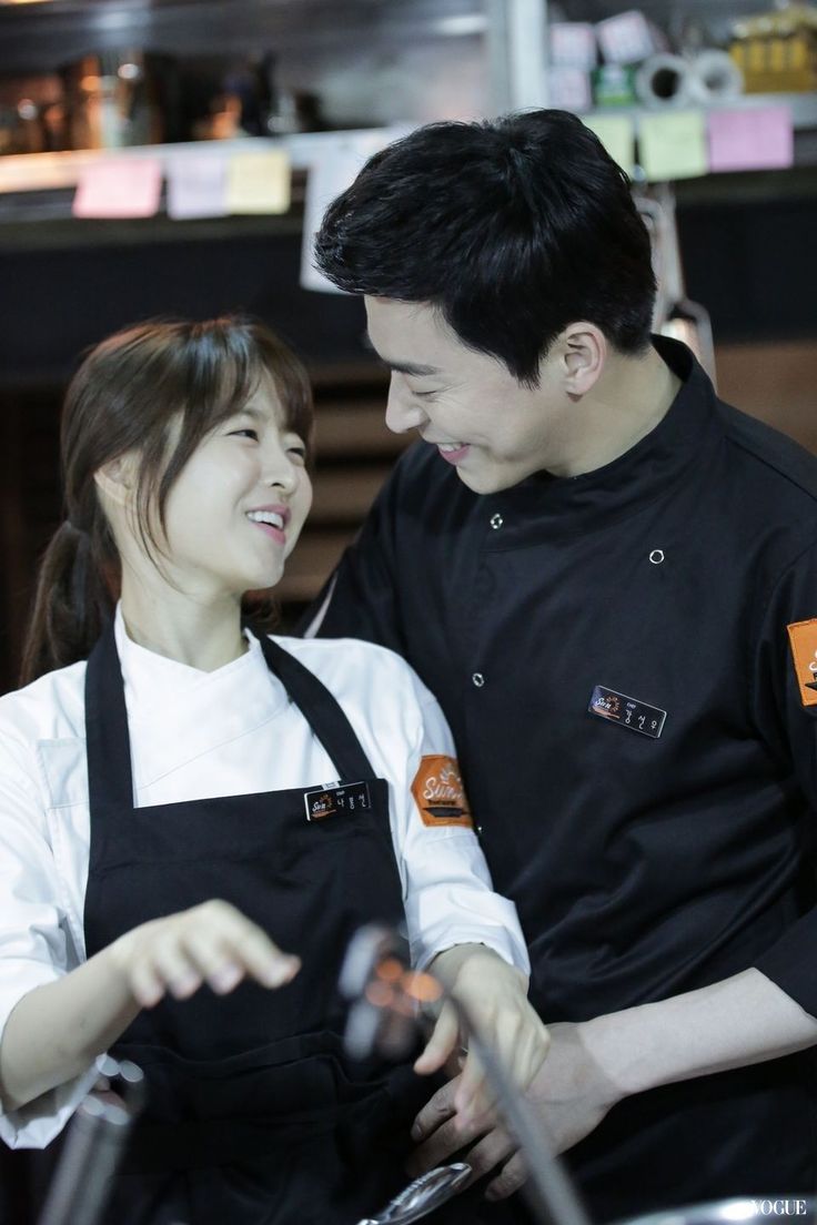 a man and woman standing next to each other in front of a frying pan